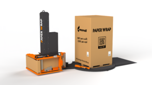 Industrial packaging setup: a tall black PAPER WRAP machine beside a large brown cardboard box on a pallet, with an orange base machinery nearby